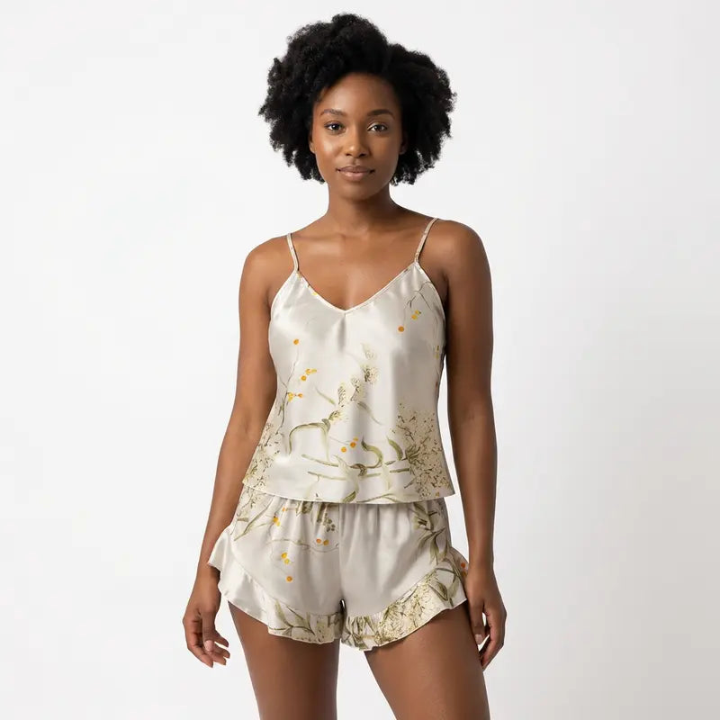 Ensemble satin blanc pour femme avec motifs floraux dorés et verts, débardeur fluide à fines bretelles et short assorti à volants.