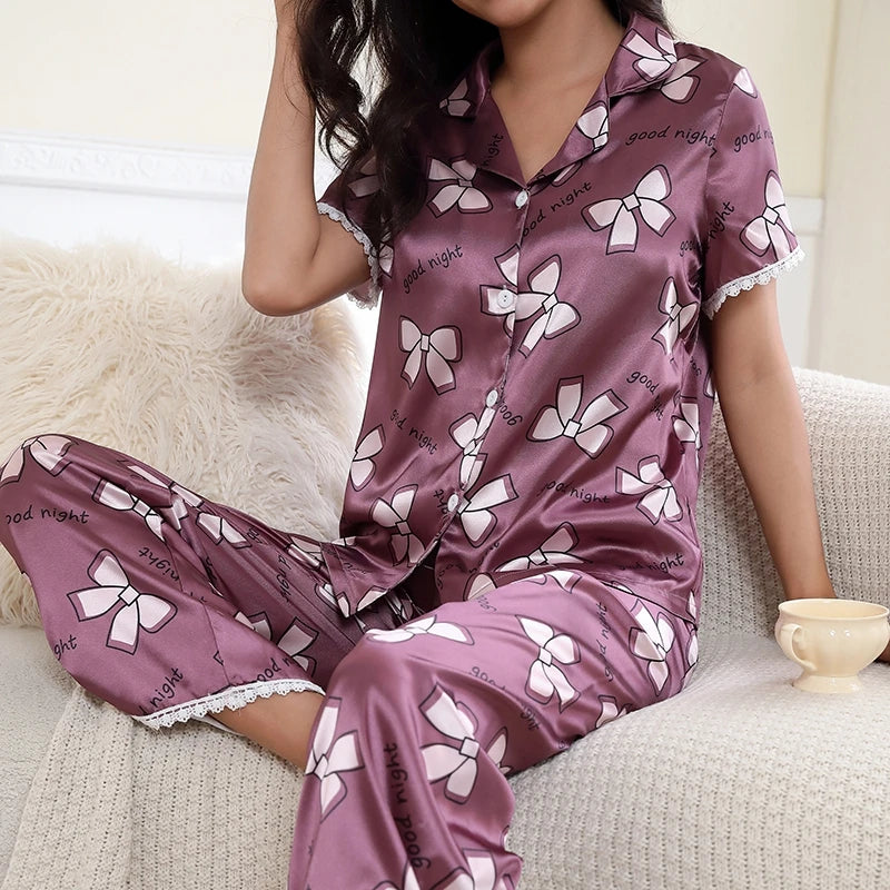 Pyjama satin mauve à motifs nœuds porté par une femme assise avec une tasse à la main.