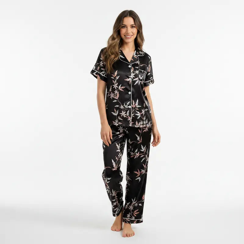 Pyjama satin femme noir à imprimé floral, composé d’une chemise manches courtes boutonnée et d’un pantalon assorti. Ensemble élégant et fluide présenté sur mannequin dans un studio au fond gris clair.