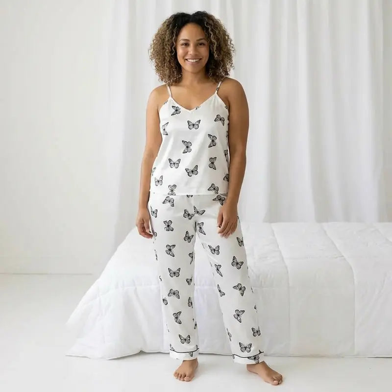Pyjama femme en satin blanc avec imprimé papillons, composé d’un débardeur à bretelles et d’un pantalon long, porté en intérieur, style confortable et élégant.