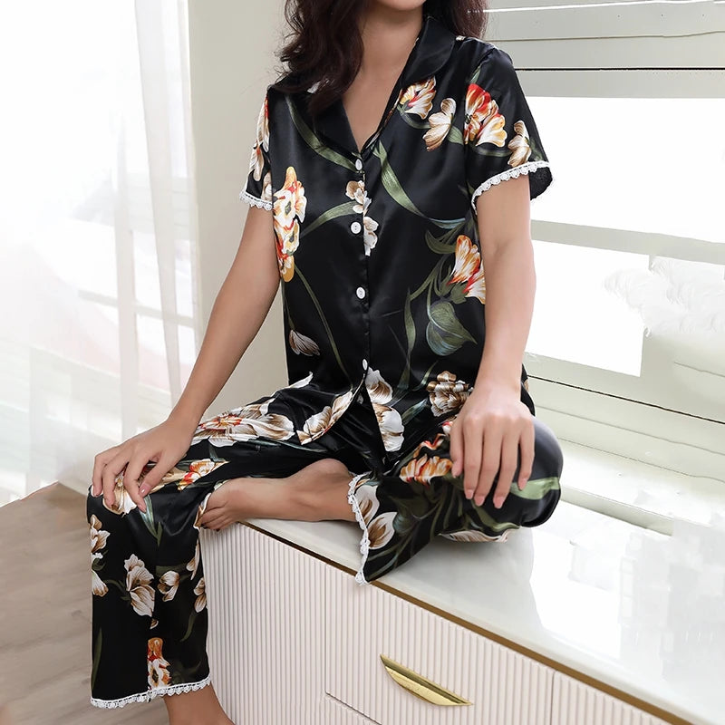 Pyjama satin noir à motifs fleuris porté par une femme assise près d’une fenêtre.